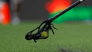a black lacrosse stick holding a lacrosse ball on a turf field